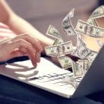 person typing with dollar bills flying
